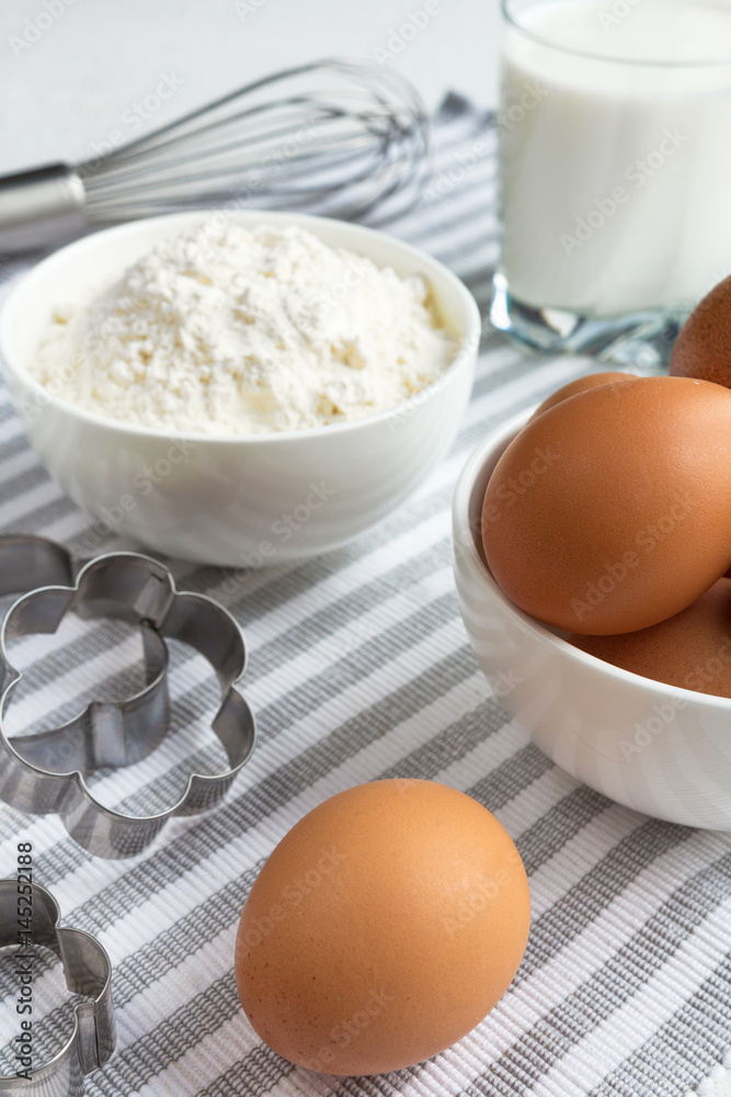 Eggs, flour and various ingredients and utensils cooking homemade cakes on the white tablecloth in blue cage concept of domestic supply Flat lay Eggs, flour and various ingredients and utensils cooking homemade cakes on the white tablecloth in blue cage concept of domestic supply Flat lay