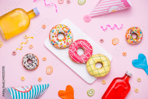 Party. Different colourful sugary round glazed donuts and bottles of drinks on pink background.
