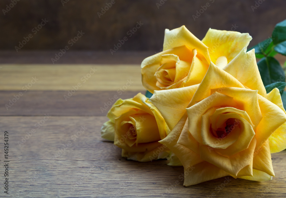 Obraz premium Bright large open yellow roses close up on oak wooden table - background