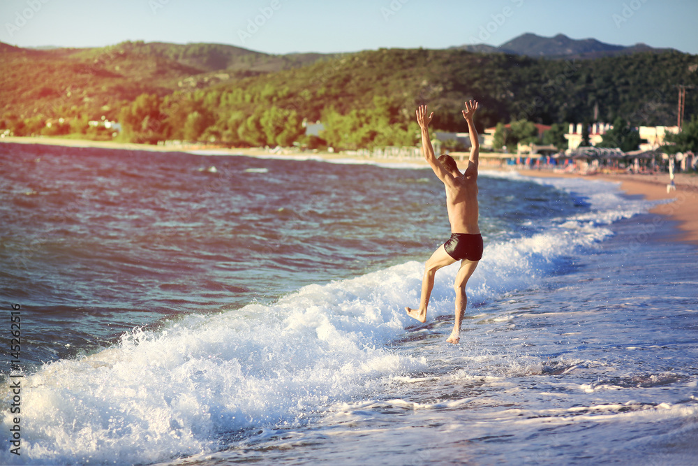 Fototapeta premium Young man jumping into the sea at sunset