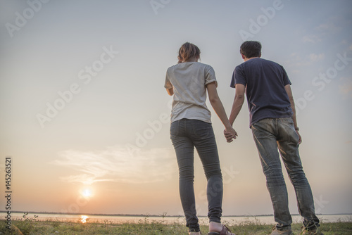 Silhouette of loving couple holding hands in heart shape over orange sunset background