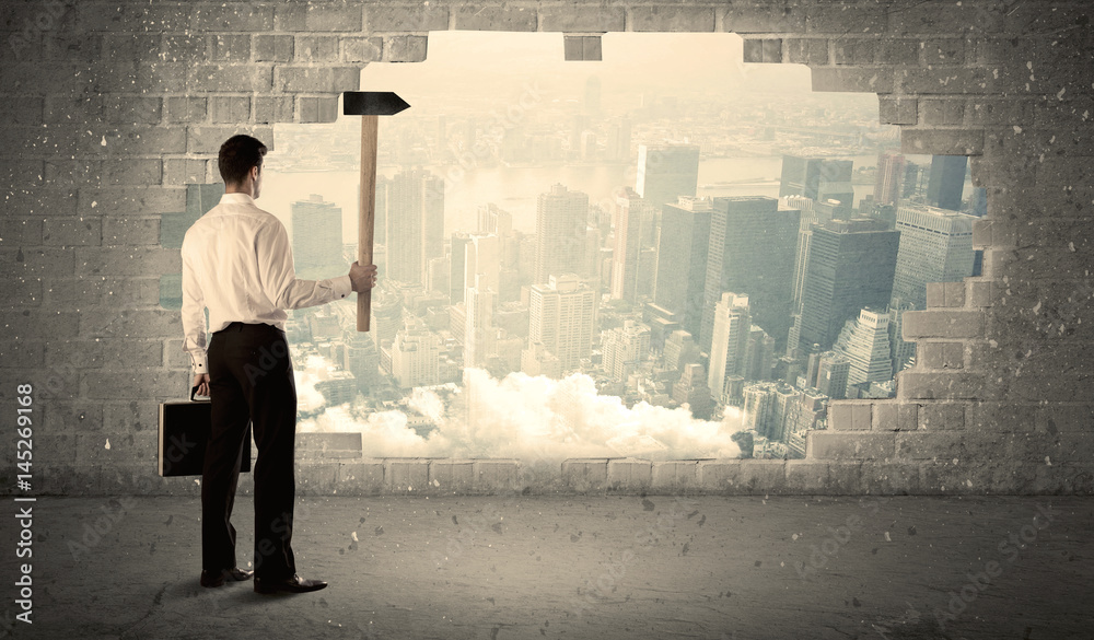 Business man hitting wall with hammer on city view Business man hitting wall with hammer on city view