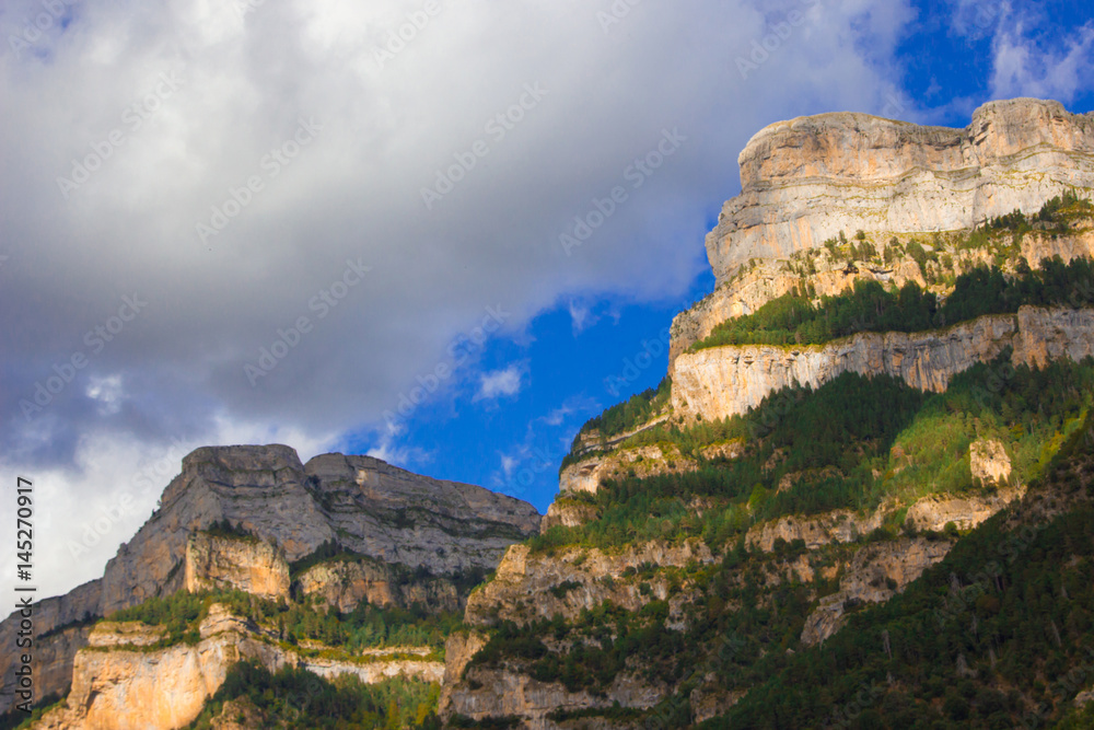 Mountain massife grey and yellow rock with green trees under blu