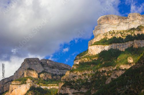 Mountain massife grey and yellow rock with green trees under blu