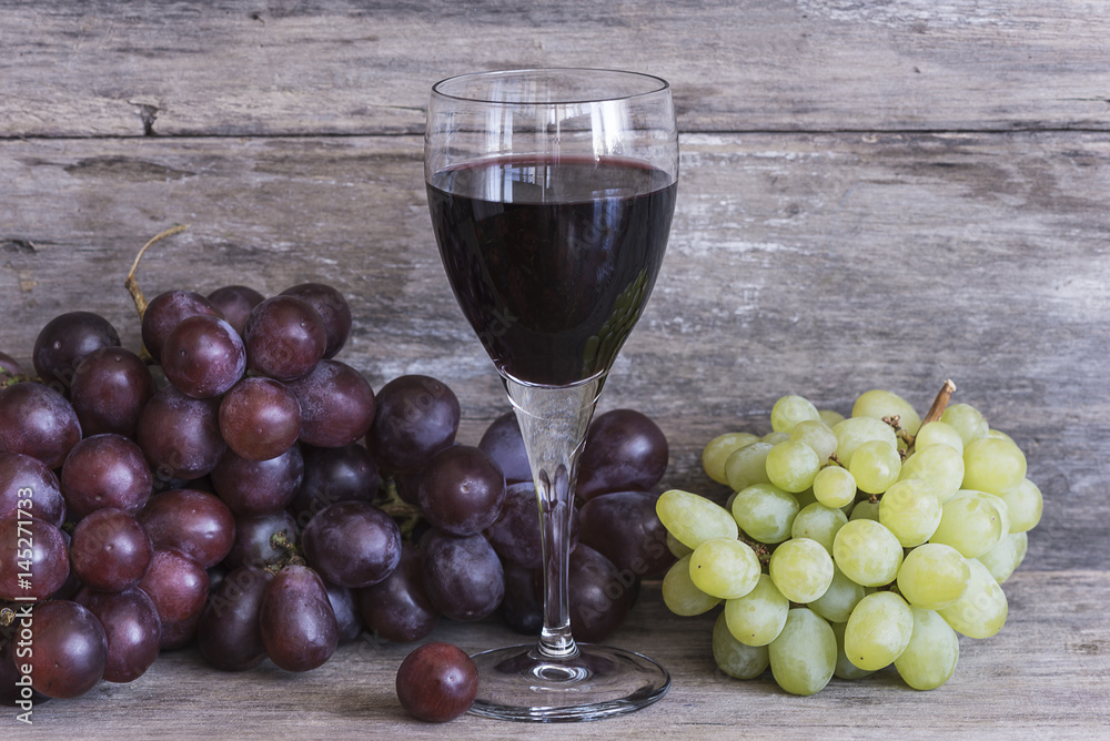 glass of red wine and red and white grapes on rustic wooden background