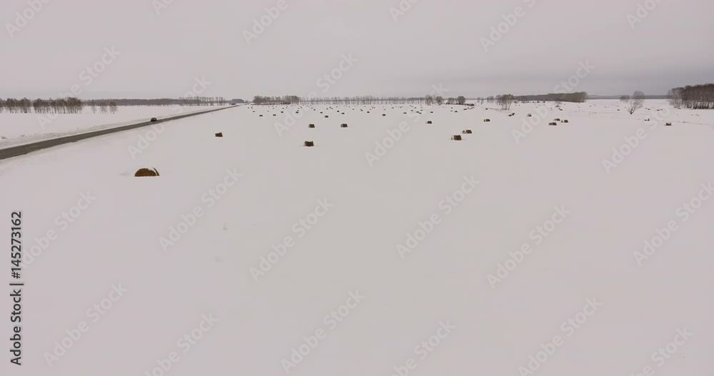 Siberia, 2017: Aerial view from helicopter: countryside in winter. A secluded road, a snowy field with haystacks. Taken from the air: movement along the winter field. Sleeping winter nature Siberia, 2017: Aerial view from helicopter: countryside in winter. A secluded road, a snowy field with haystacks. Taken from the air: movement along the winter field. Sleeping winter nature