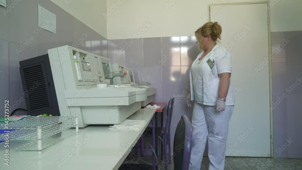 Laboratory technician monitors the operation of the analyzers for coagulation analysis, dolly shot, room interior Laboratory technician monitors the operation of the analyzers for coagulation analysis, dolly shot, room interior