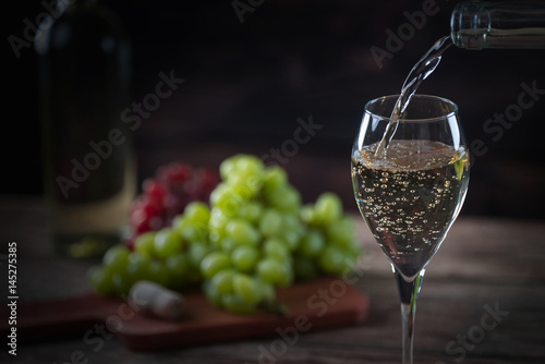 Pouring  glass of wine from a bottle of the wineglasses over rustic brown wooden background with copy space