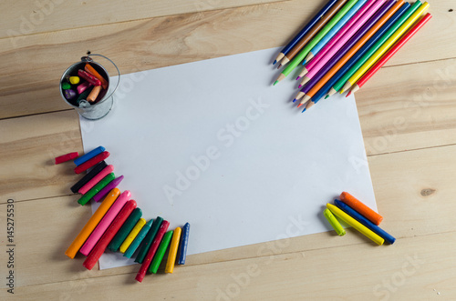 Wax crayons on white sheet, wooden background