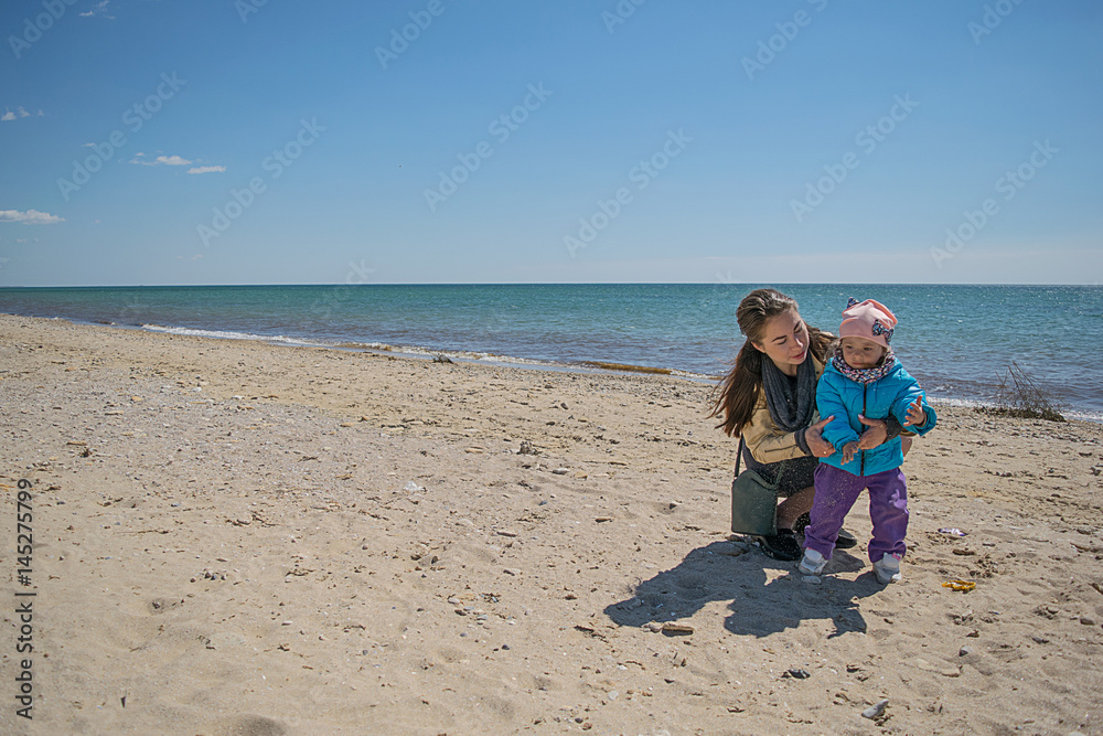 Mom and daughter are playing on the beach in the spring, molding from sand Mom and daughter are playing on the beach in the spring, molding from sand