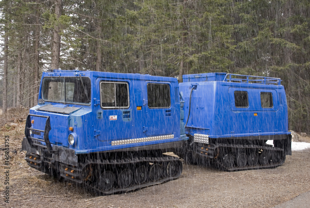 small snowcat with second wagon attached to the trailer coupling, electric blue, used to transport people in mountain huts, photographed in early spring, during snowfall, Trentino Alto Adige, Italia small snowcat with second wagon attached to the trailer coupling, electric blue, used to transport people in mountain huts, photographed in early spring, during snowfall, Trentino Alto Adige, Italia