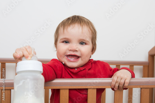 Adorable baby playing on a bed and drinking milk from a bottle
