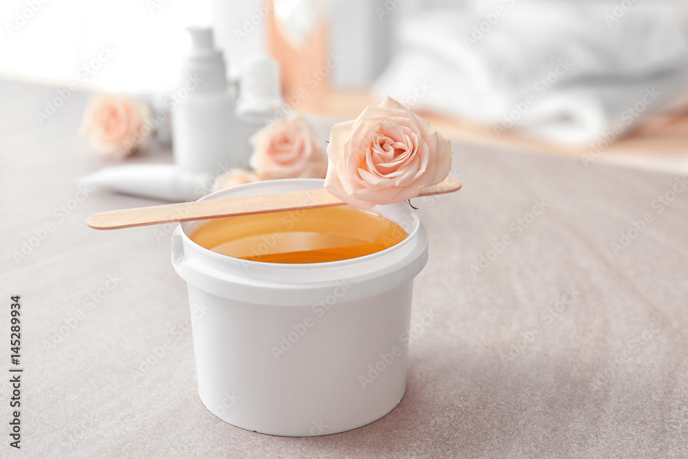 Plastic bucket with sugaring paste, wooden stick and flower on table Plastic bucket with sugaring paste, wooden stick and flower on table