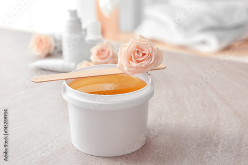 Plastic bucket with sugaring paste, wooden stick and flower on table