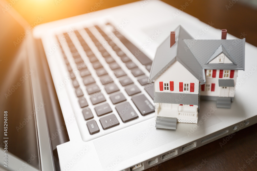 Miniature House And Laptop Computer Resting on Desktop. Miniature House And Laptop Computer Resting on Desktop.