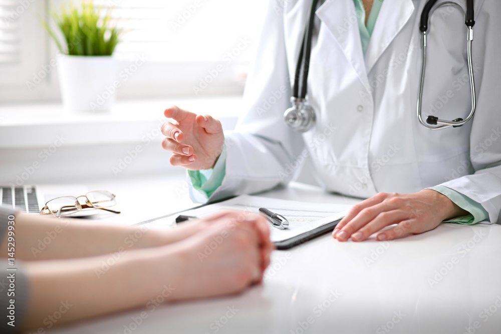 Close up of doctor and patient sitting at the desk near the window in hospital Close up of doctor and patient sitting at the desk near the window in hospital
