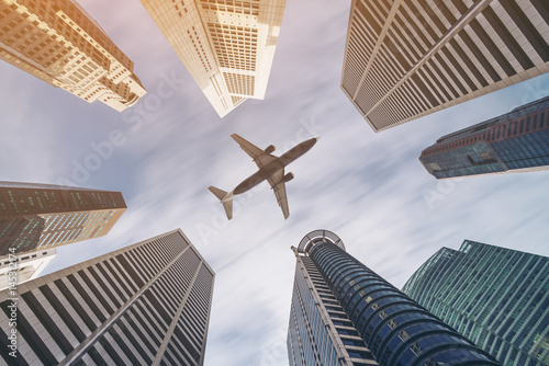 Fotografie Airplane flying over city business buildings, high-rise skyscrapers