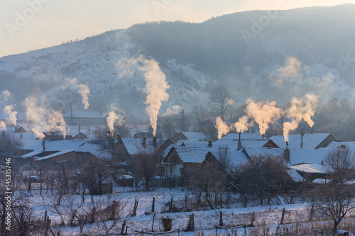 Beautiful winter scenery with smoke coming from house chimneys, on a bright, cold, morning, in remote countryside in Europe