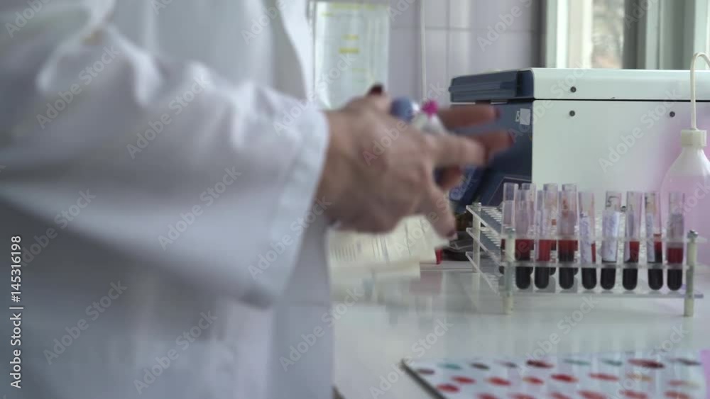 Laboratory desk with blood samples in test tubes, analysis and paper work, hands close up, room interior, daylight, steady cam shot Laboratory desk with blood samples in test tubes, analysis and paper work, hands close up, room interior, daylight, steady cam shot