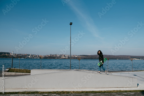 Pretty teen girl spending time in the park near the water with his skate