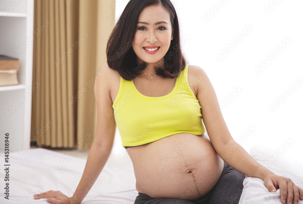 asian pregnant woman smiling while sitting on bed
