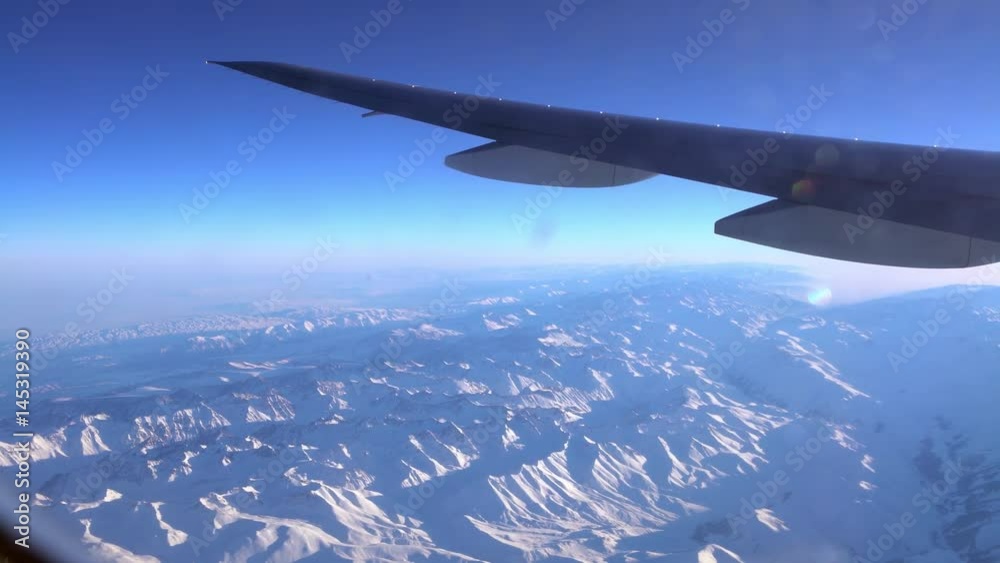 4K Traveling by air. Wonderful view of the Tian Shan snow mountains and clouds with blue sky from above in Central Asia, as seen through an airplane window-Dan 4K Traveling by air. Wonderful view of the Tian Shan snow mountains and clouds with blue sky from above in Central Asia, as seen through an airplane window-Dan