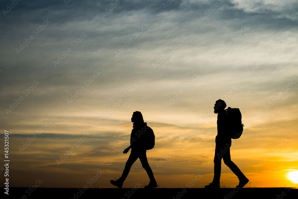 Silhouettes of two hikers with backpacks enjoying sunset. Travel concept.