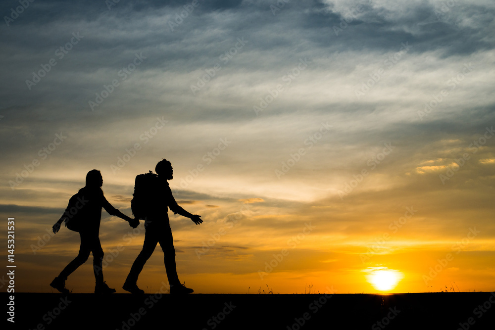 Silhouettes of two hikers with backpacks enjoying sunset. Travel concept.