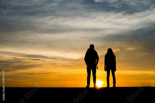 Silhouettes of two hikers with backpacks enjoying sunset. Travel concept.