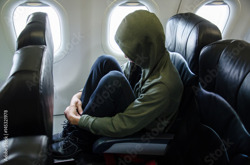 Lonely man wear green hood and Airplane Seat View Interior. Black Cover with Light from Window. © migrean