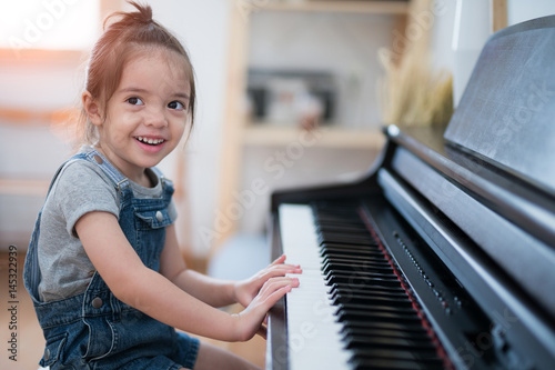 Fototapeta Little girl play piano and sing a song in living room