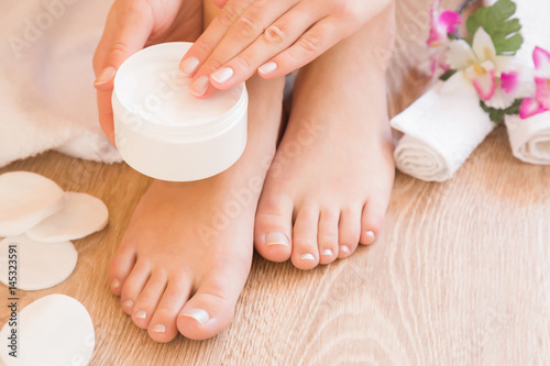 Young woman's hands holding a jar of foot moisturizing cream. Pedicure beauty salon.