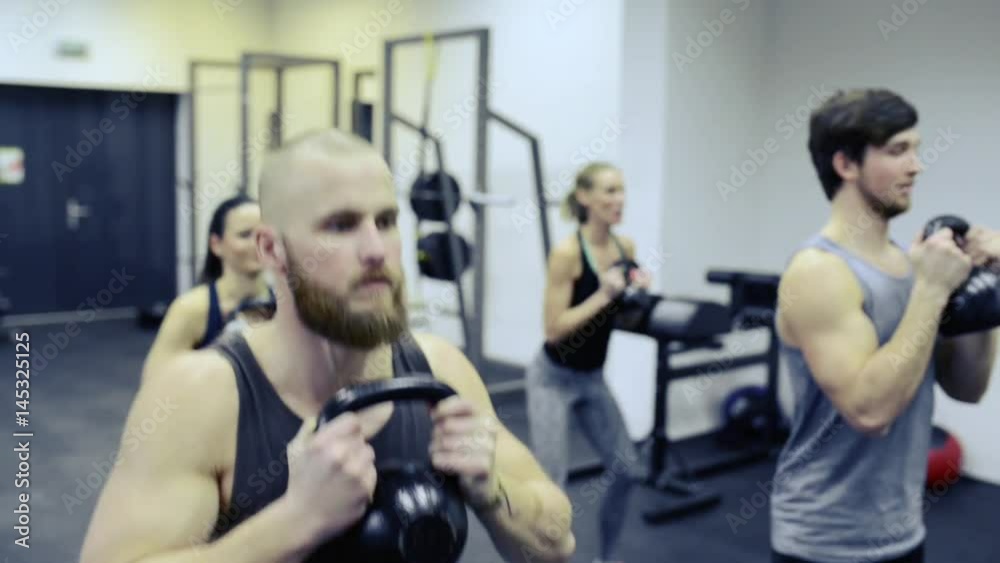 Young people in crossfit gym doing squats with kettlebells Young people in crossfit gym doing squats with kettlebells