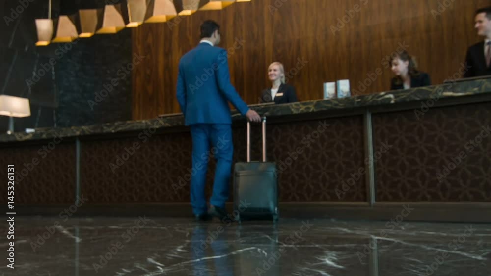 Businessman with suitcase walking to reception desk