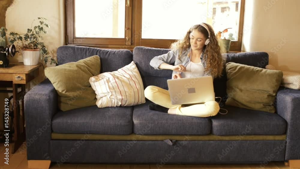 Beautiful teenage girl at home sitting on couch, laptop on her lap, wearing headphones, listening music. Beautiful teenage girl at home sitting on couch, laptop on her lap, wearing headphones, listening music.