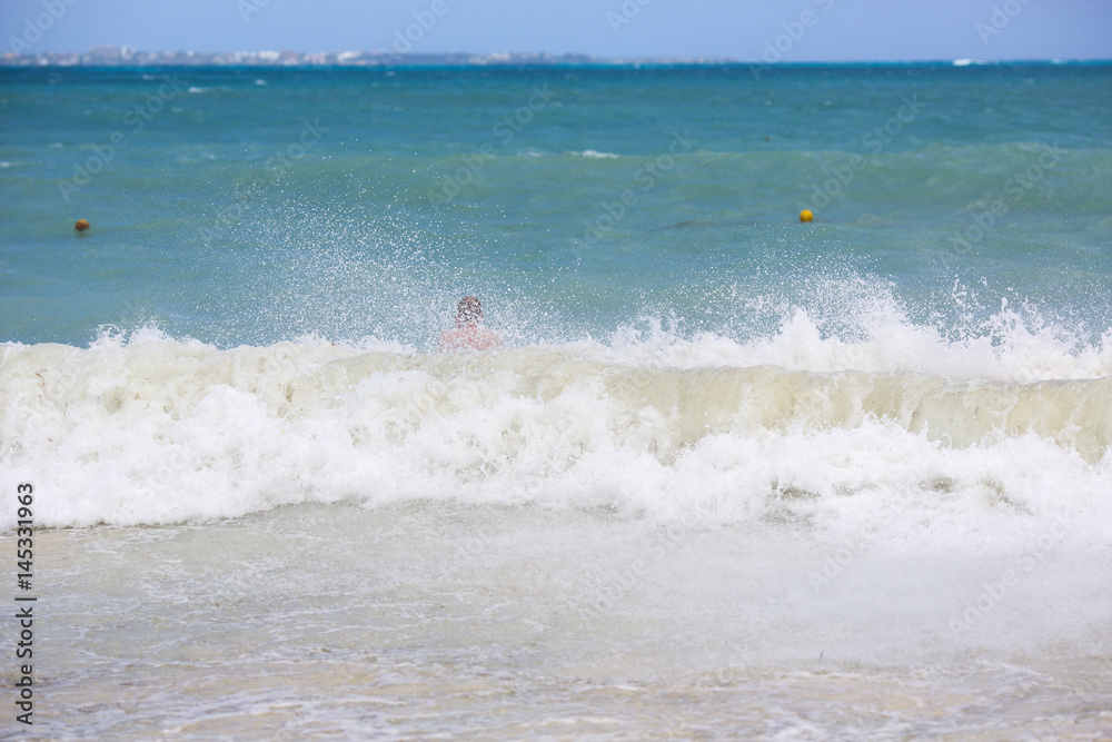 Big wave on the sea. A swimmer in the background out of focus.