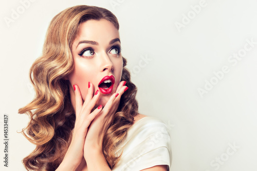Shocked and surprised girl screaming and  looking to the side presenting  your product . Woman amazed .Beautiful girl  with curly hair and red nails manicure. Expressive facial expressions photo
