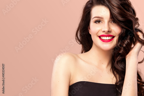 Smiling wwith long and shiny wavy hair . Beautiful model, curly hairstyle on orange background. photo