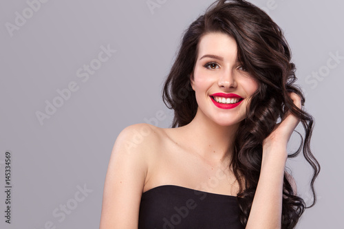 Smiling Woman with long and shiny wavy hair . Beautiful model, curly hairstyle on gray background.