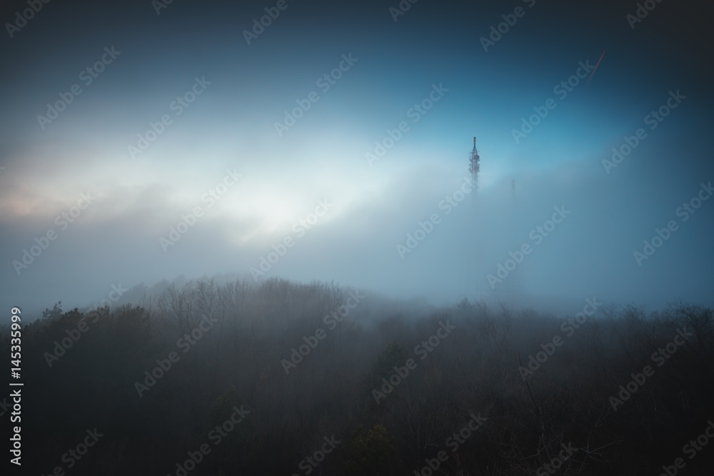 Misty fog over connection and radio tower in the mountain