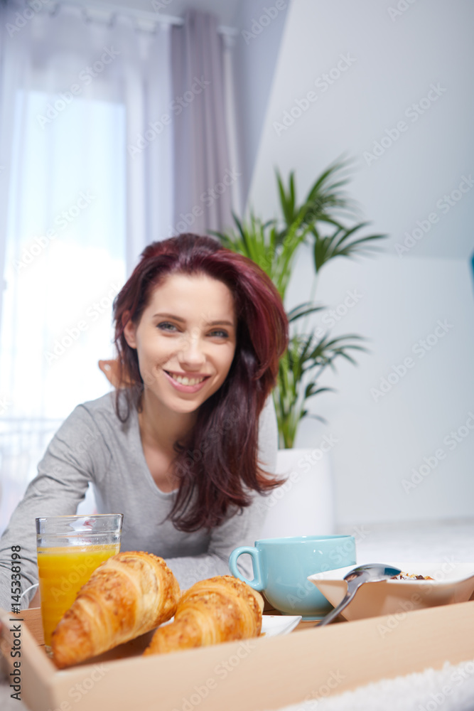 Happy brunette having breakfast in bed at home in bedroom