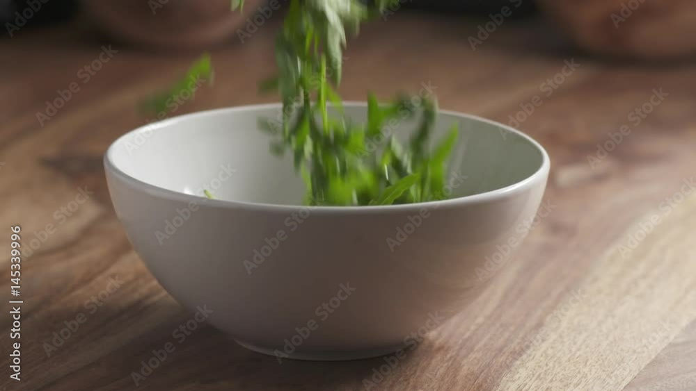 Slow motion of washed arugula leaves falling into the bowl on wooden table, 180fps prores footage Slow motion of washed arugula leaves falling into the bowl on wooden table, 180fps prores footage