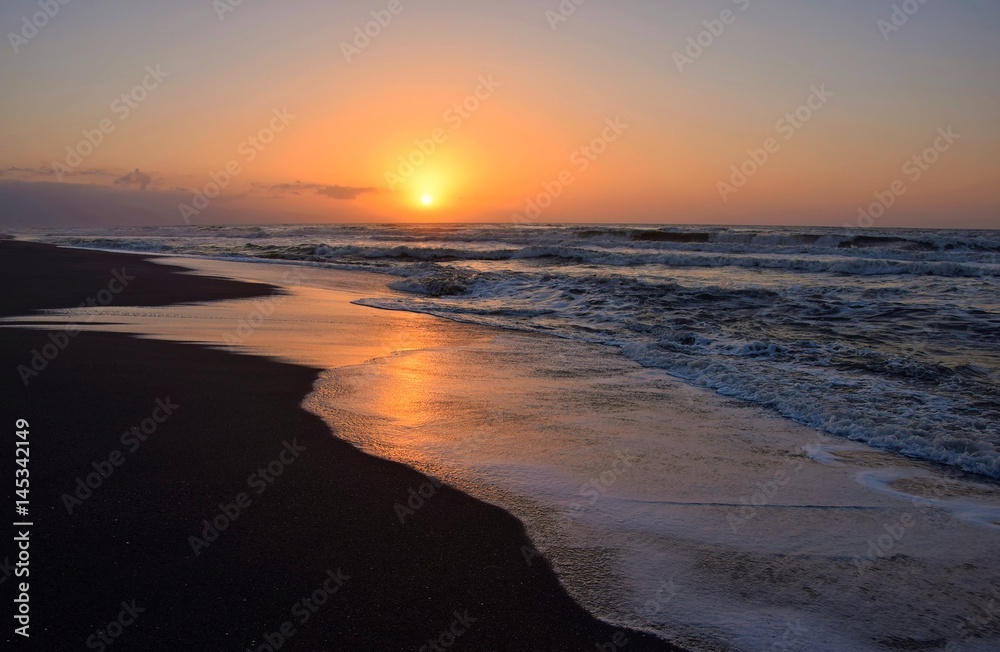 Amanecer en la playa, observándose en el horizonte la salida del sol y un bonito cielo con diferentes tonalidades que se reflejan en el agua de la orilla del mar