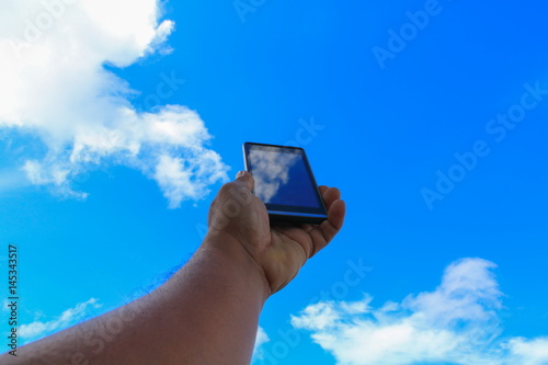 male hand holding mobile phone closeup or smartphone on blue sky background