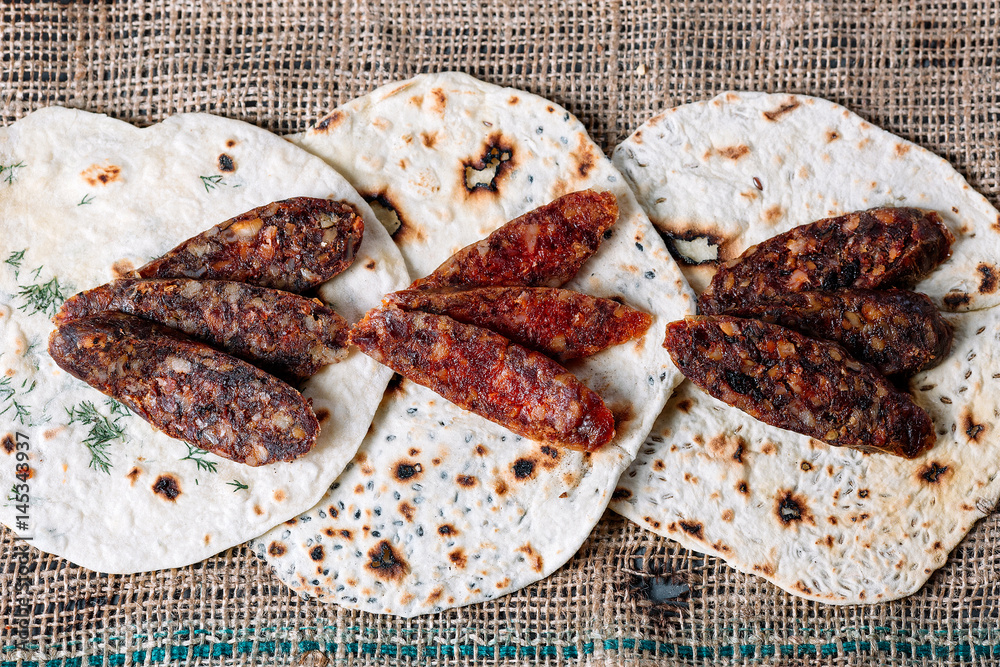Three pitas with pieces of salami on a wooden cutting board on a brown canvas Three pitas with pieces of salami on a wooden cutting board on a brown canvas