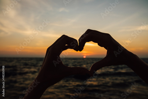 Silhouette hand in heart shape with sunrise in the middle and beach background