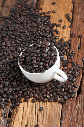 Close up shot of dark roasted coffee bean in white ceramic cup on wooden floor with copy space
