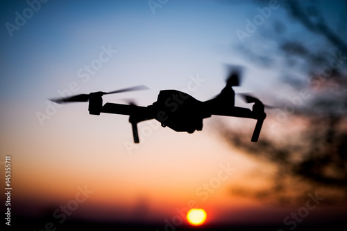 Fototapeta Naklejka Na Ścianę i Meble -  Flying drone into the sunset. Silhouette against sun. Quad copter in motion.