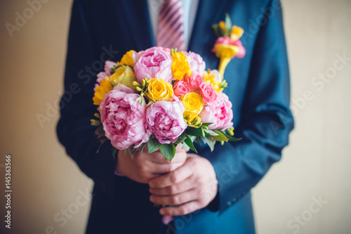 Groom hand holding bouquet fresh flowers
