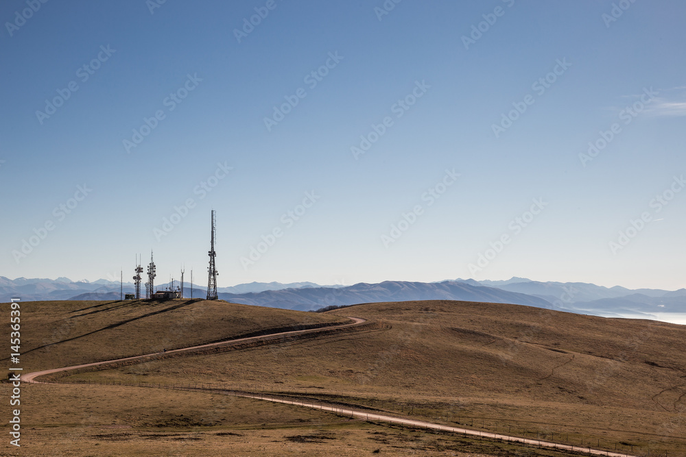 A curvy road towards some antennas on a top of mountain, under a blue, empty sky